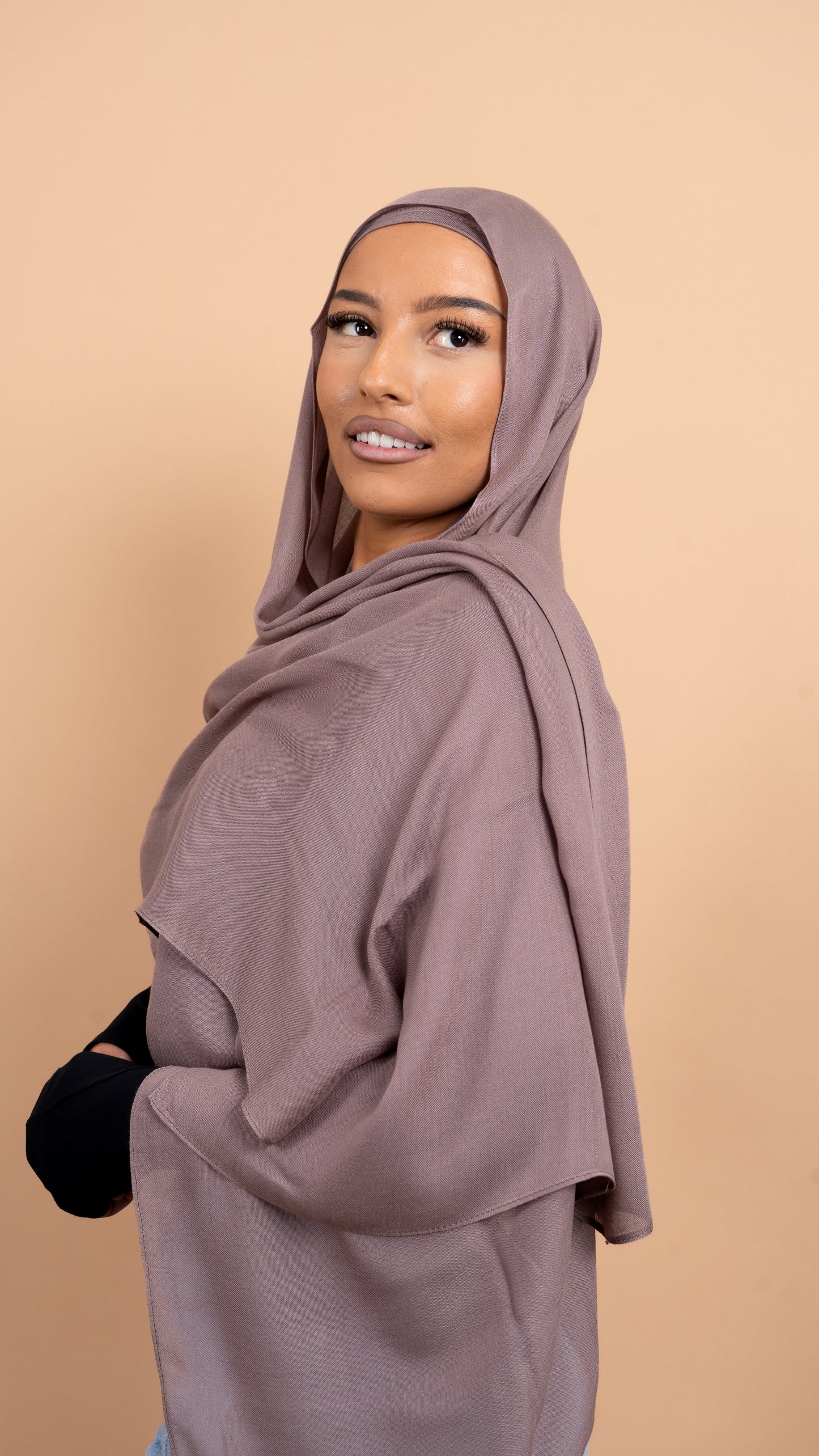 Femme maghrébine voilée avec un foulard en modal de couleur taupe. Photo sur fond beige uni.