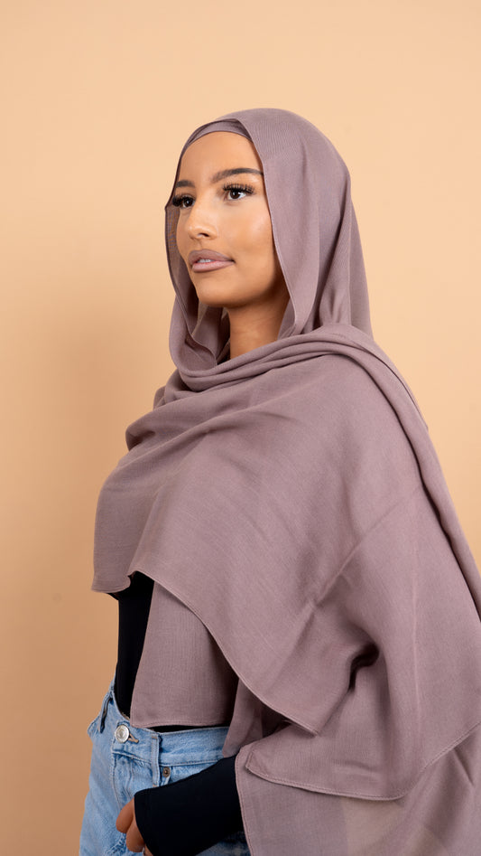 Femme maghrébine voilée avec un foulard en modal de couleur taupe. Photo sur fond beige uni.