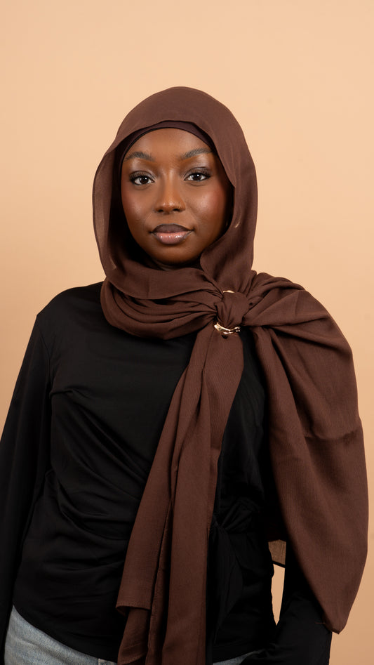 Femme noire voilée avec un foulard en modal de couleur marron. Photo sur fond beige uni.