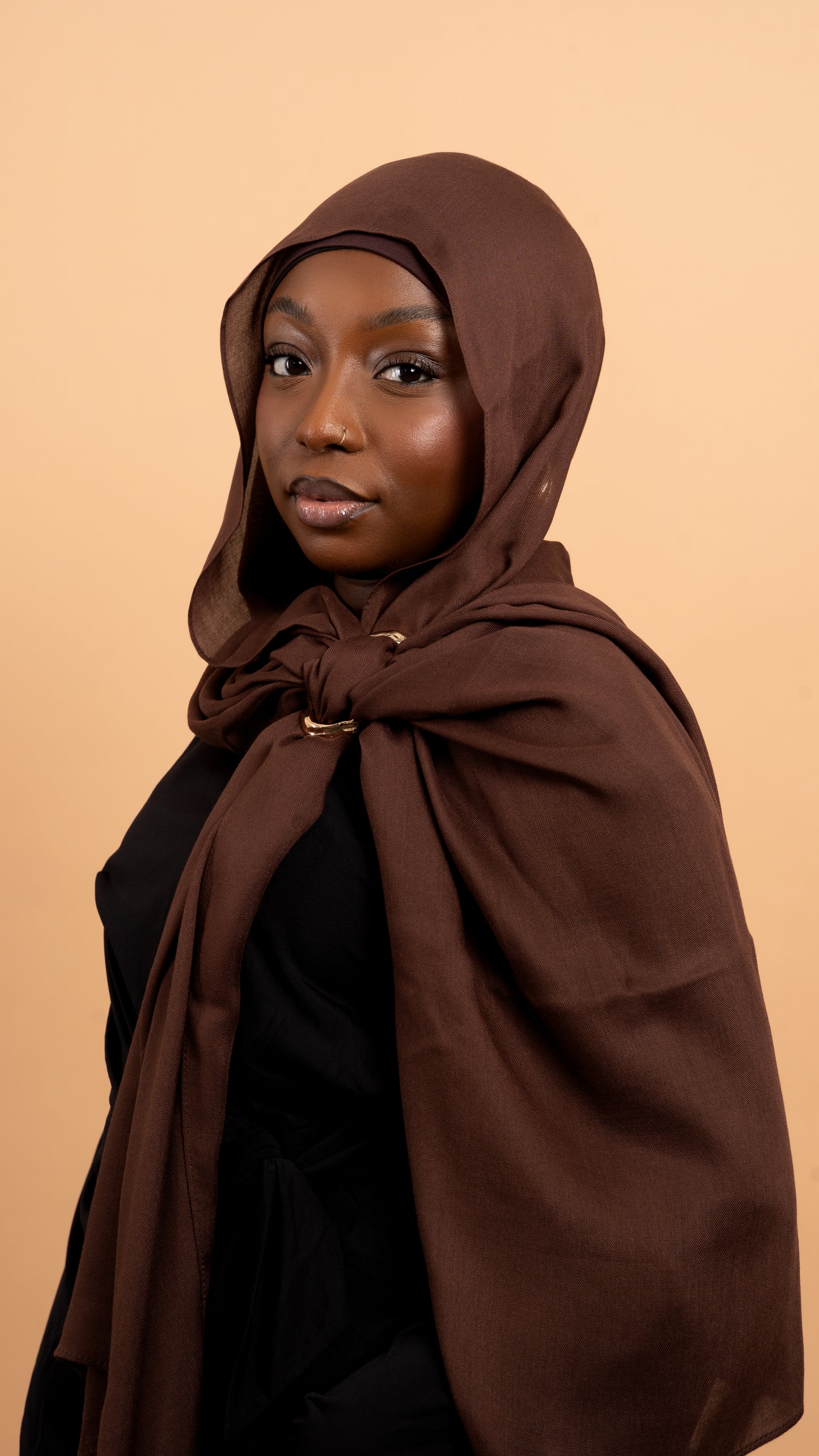Femme noire voilée avec un foulard en modal de couleur marron. Photo sur fond beige uni.