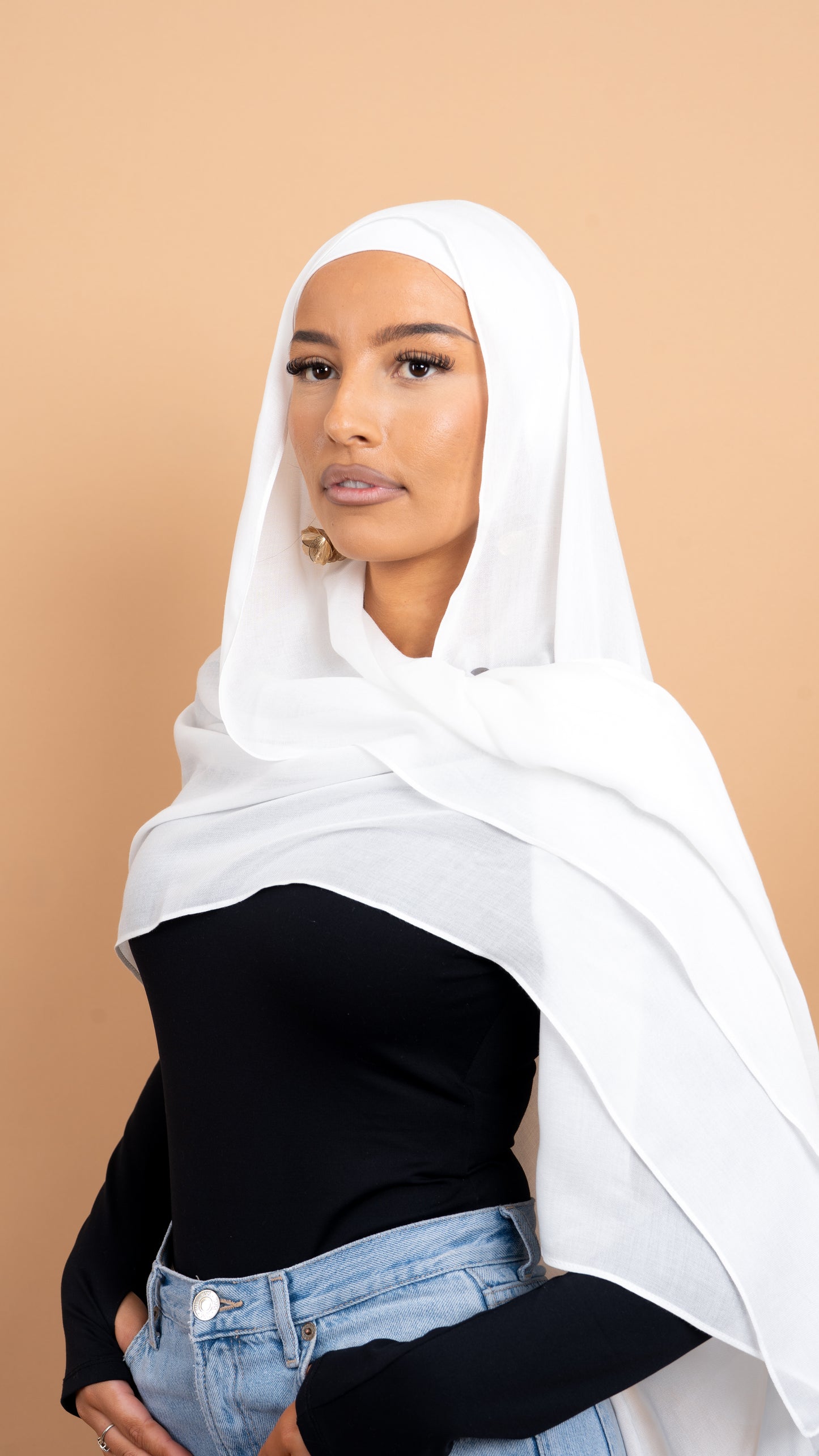 Femme maghrébine voilée avec un foulard en modal de couleur blanc. Photo sur fond beige uni.