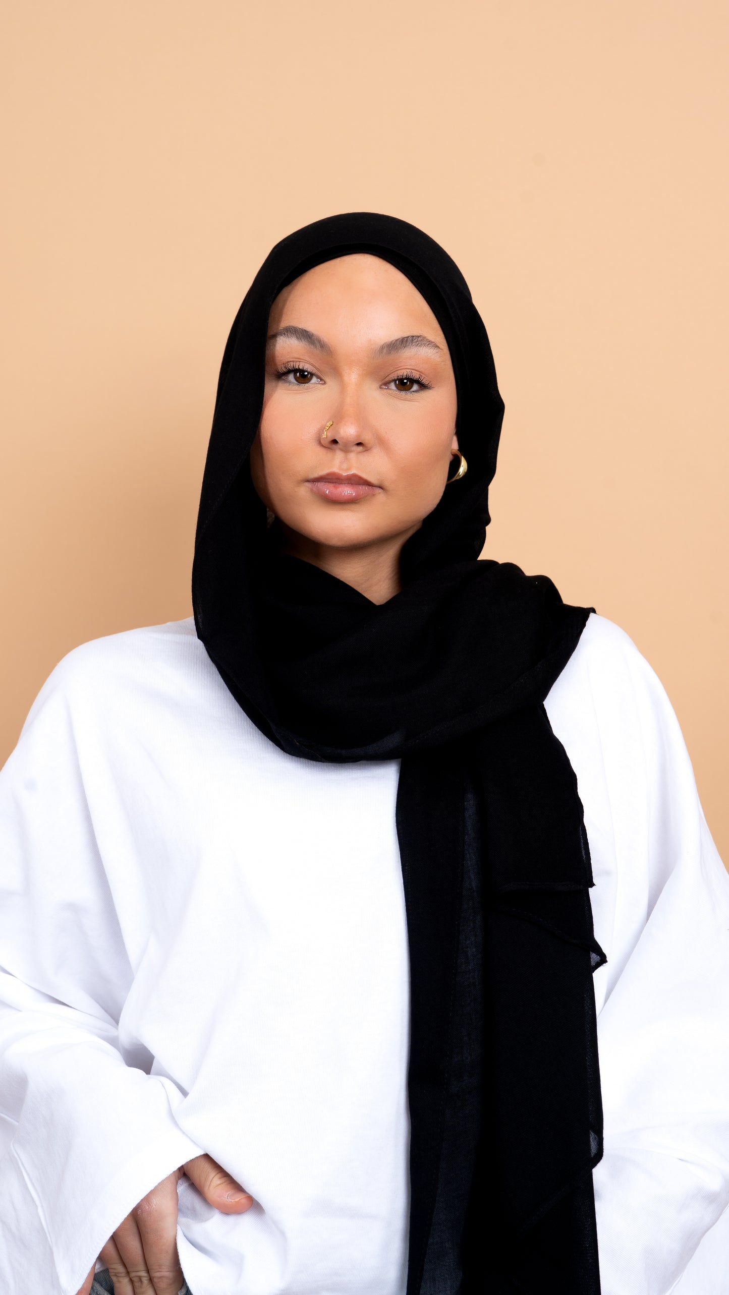 Femme blanche voilée avec un foulard en modal de couleur noir. Photo sur fond beige uni.