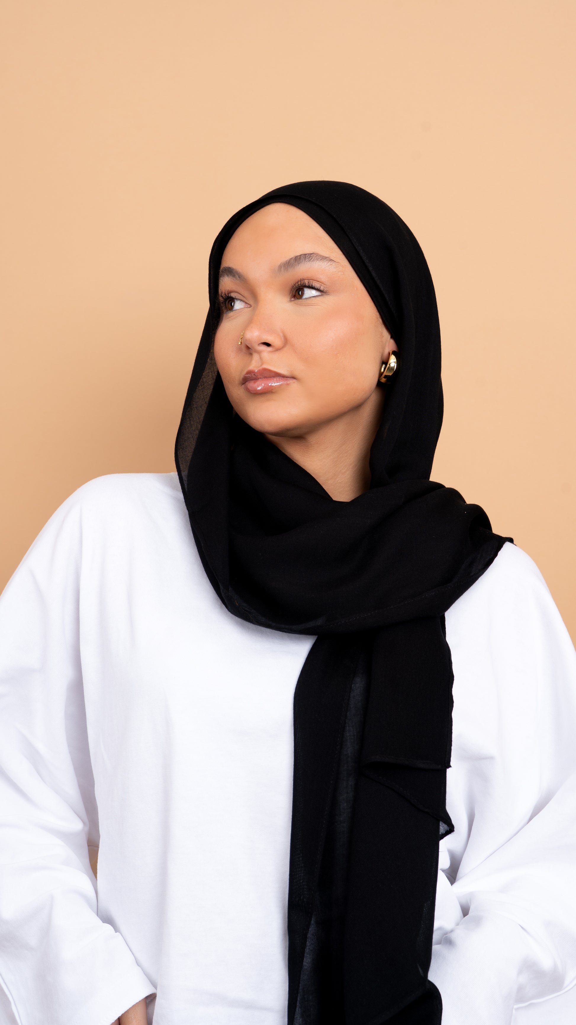 Femme blanche voilée avec un foulard en modal de couleur noir. Photo sur fond beige uni.