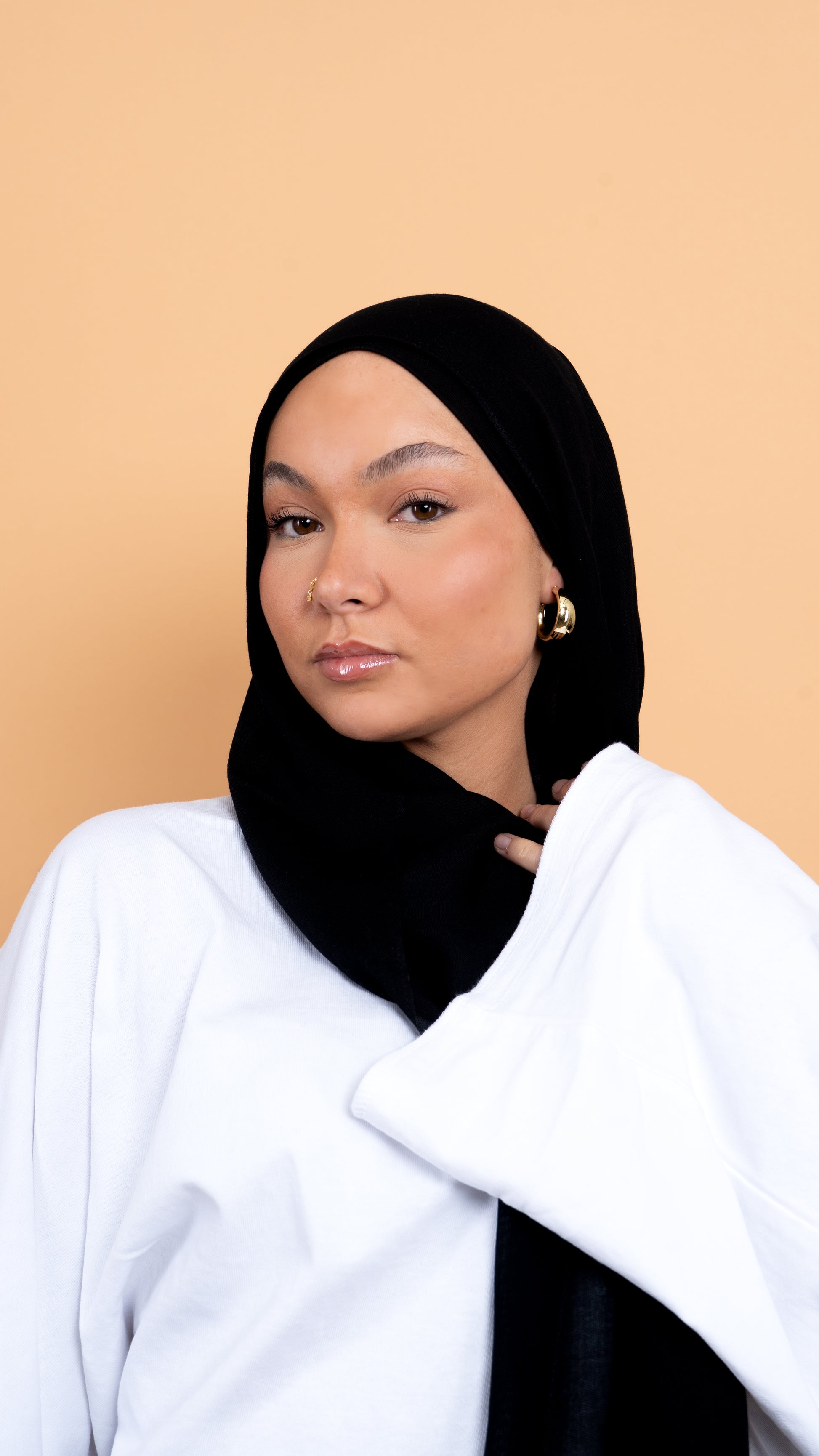 Femme blanche voilée avec un foulard en modal de couleur noir. Photo sur fond beige uni.