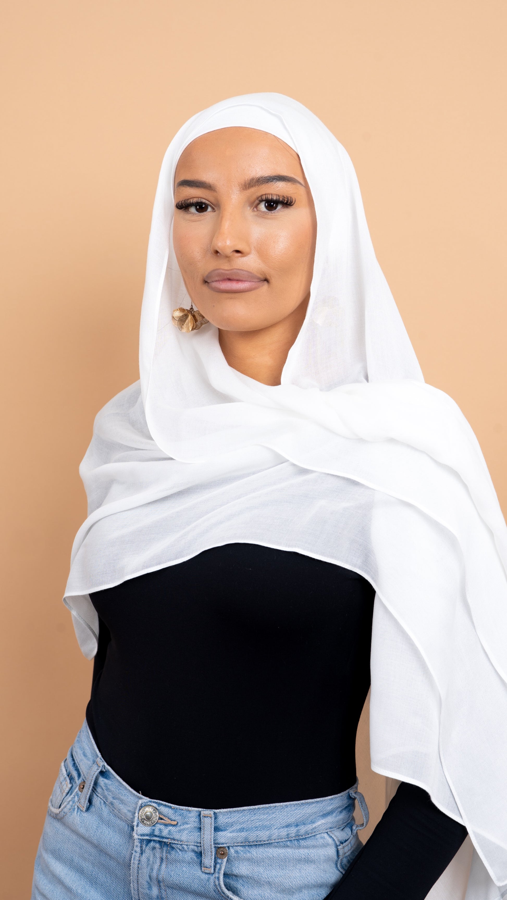 Femme maghrébine voilée avec un foulard en modal de couleur blanc. Photo sur fond beige uni.