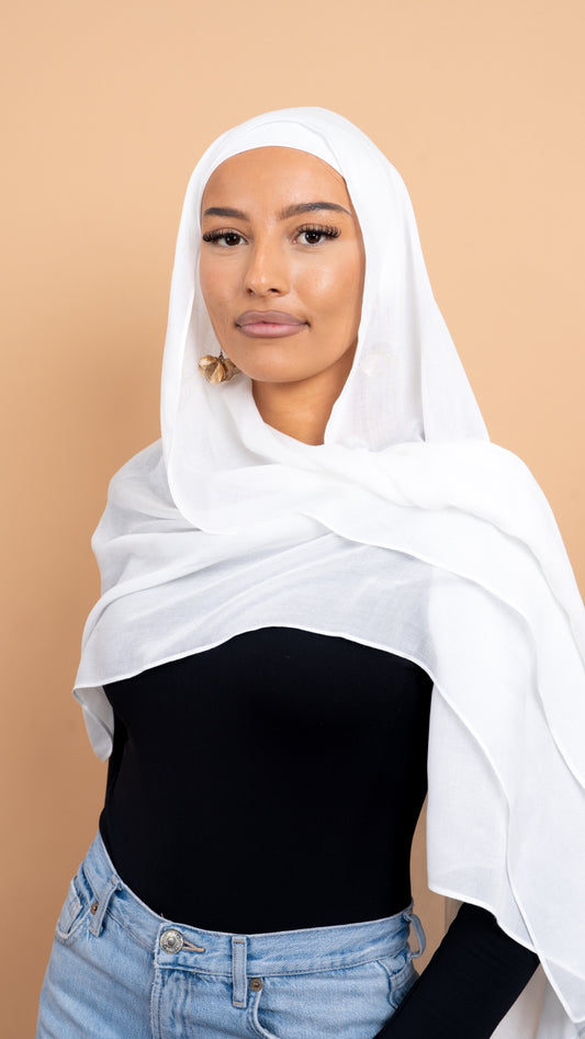 Femme maghrébine voilée avec un foulard en modal de couleur blanc. Photo sur fond beige uni.