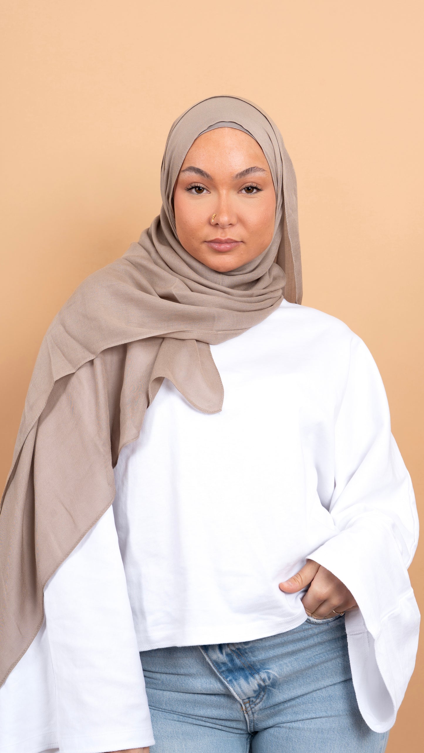 Femme blanche voilée avec un foulard en modal de couleur gris. Photo sur fond beige uni.